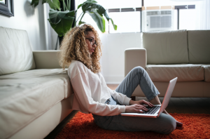 Woman sitting on floor near couch using a laptop