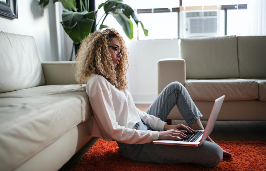 Woman sitting on floor near couch using a laptop