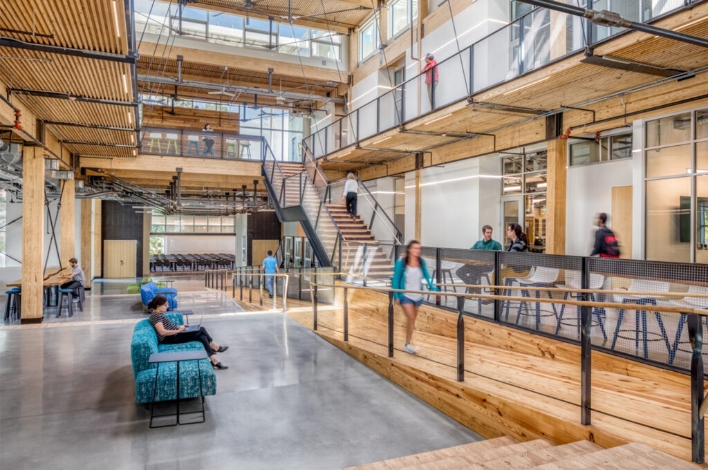 Bright multi level open concept common area with wooden beams stairs and people sitting or walking around