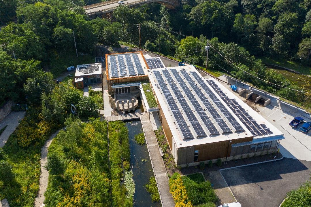 Aerial view of a building with solar panels on the roof surrounded by trees and a water feature nearby