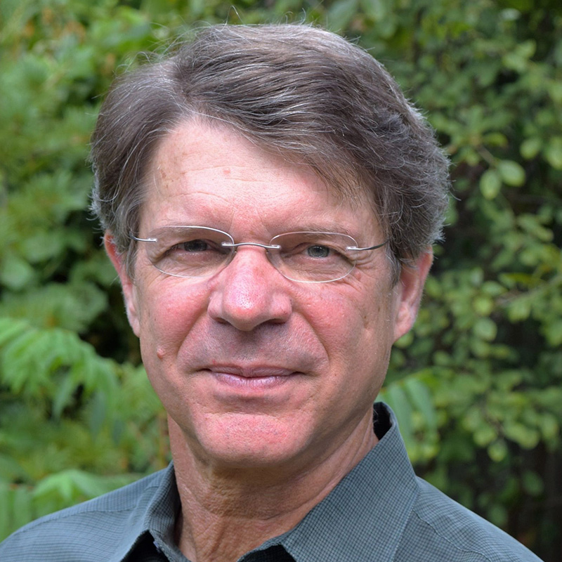 Portrait of a middle aged man with glasses outdoors neutral expression green foliage background