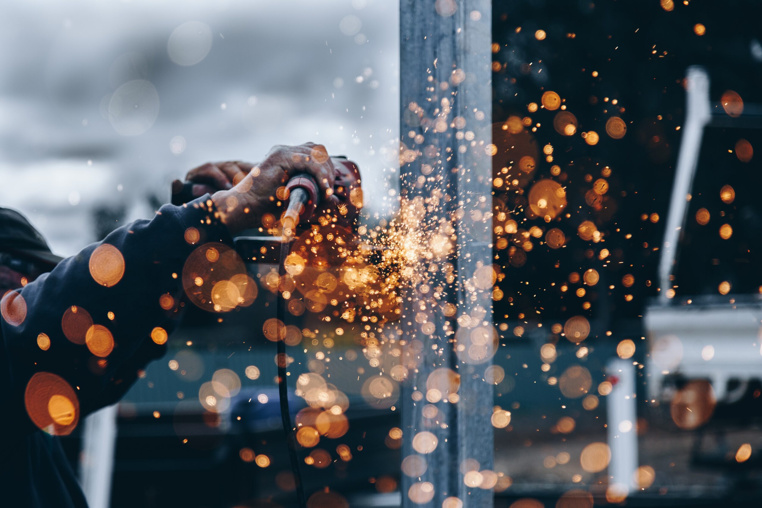 Christopher burns 8kfcr12oeum unsplash 1 | trim tab Close up of hands operating a grinder sparks flying as metal is cut or ground in a workshop setting