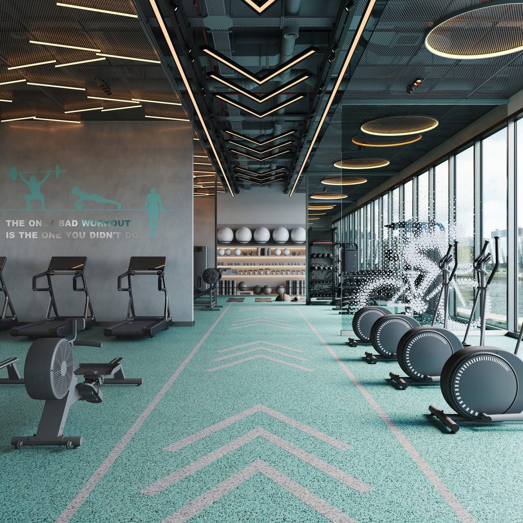 Modern gym interior with cardio machines in foreground weight racks and shelves in the back and large circular ceiling lights wall displays the motivational quote'The only bad workout is the one you didn't do.'